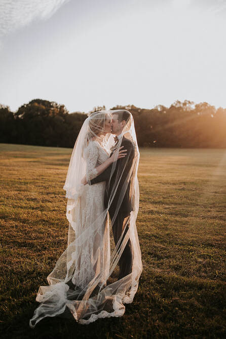 couple kiss at sunset underneath bridal veil