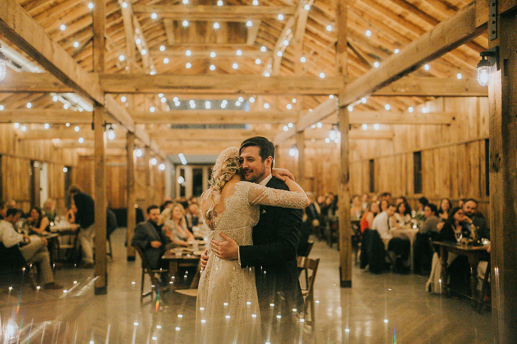 couple's first dance under string lights in barn wedding venue