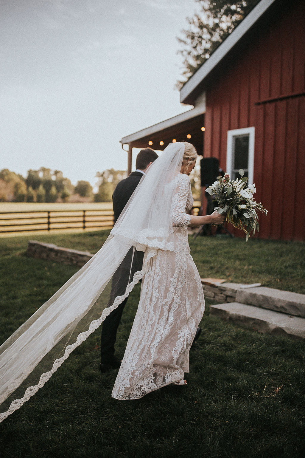 couple walks towards red barn at Nashville wedding venue